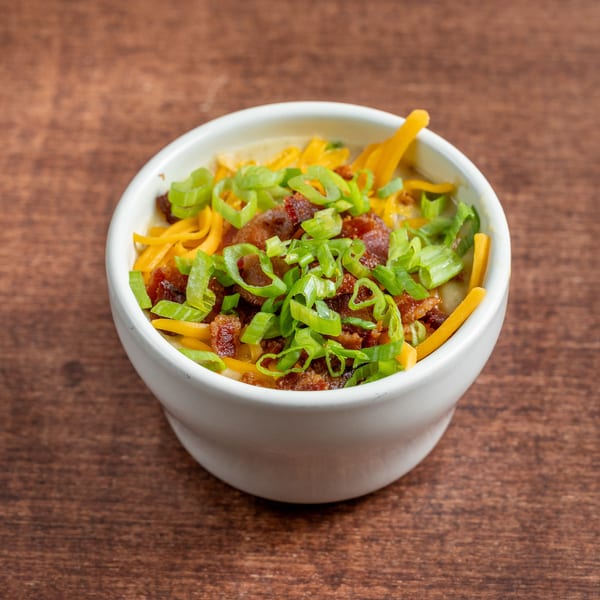 Loaded creamy soup in a white bowl, garnished with cheddar, bacon, and green onions.
