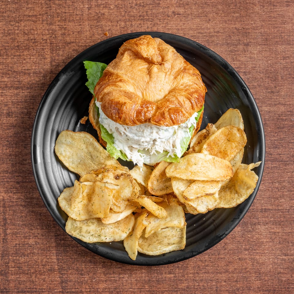 Croissant chicken salad sandwich with lettuce and potato chips on a black plate.