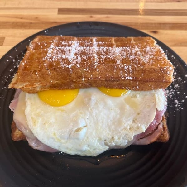 A waffle sandwich with ham, cheese, and two fried eggs, dusted with powdered sugar.