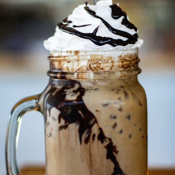 Iced coffee in a mason jar mug, topped with whipped cream and chocolate drizzle.